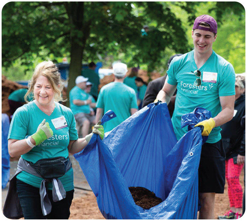 Foresters members woman and man carrying bag to help build a playground as part of Foresters purpose